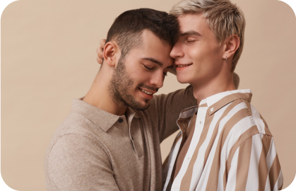 Stock photo of 2 men embracing closely, smiling with eyes closed, against a beige background for a gay hookup.